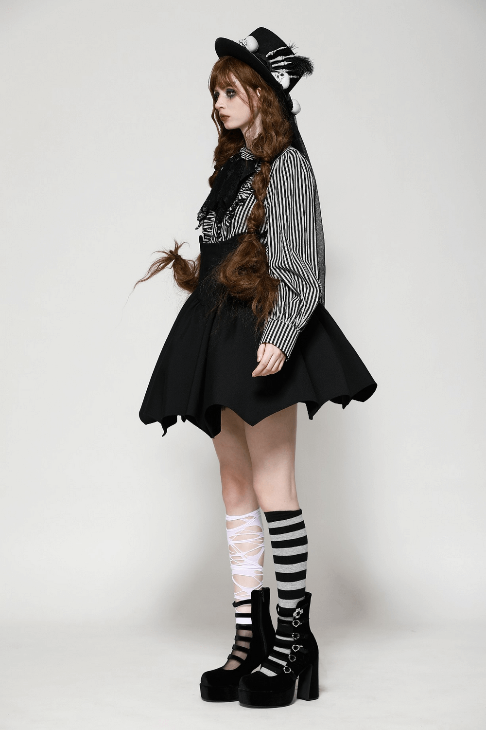 Side view of a model in a striped gothic blouse, black skirt, and striped socks, showcasing a stylish gothic outfit.