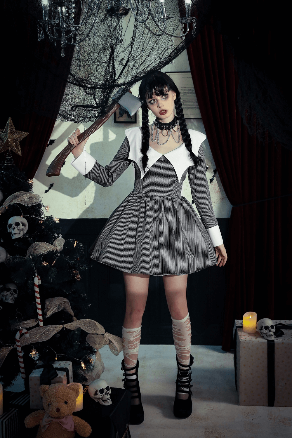 Stylish girl in striped dress with white collar, holding an axe, standing in a spooky decorated room.