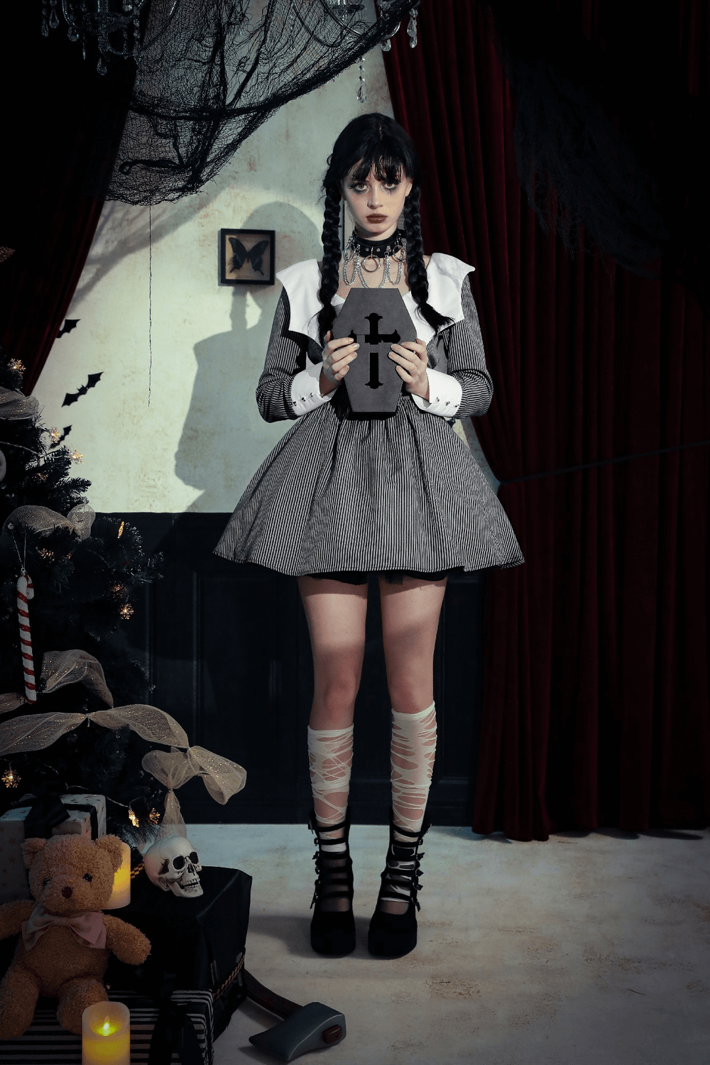 Girl in a gray dress with white collar holding a cross, set in a spooky room with candles and decorations.