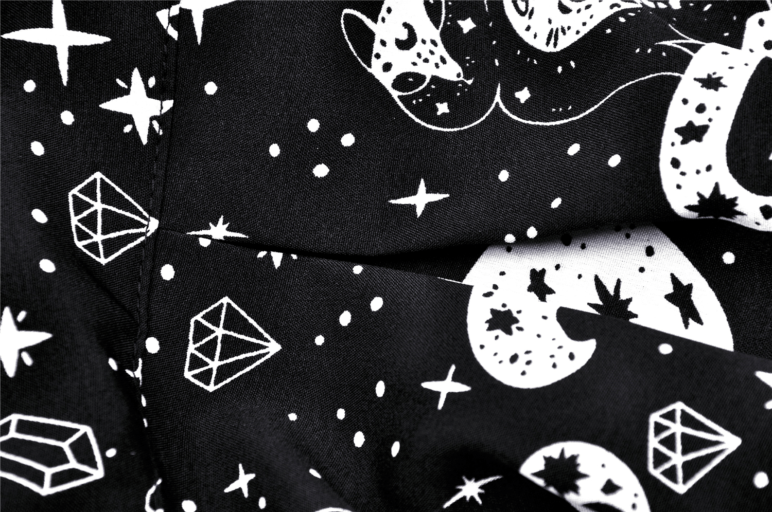 Close-up of black fabric with whimsical white stars, moons, and cat print for gothic punk fashion.