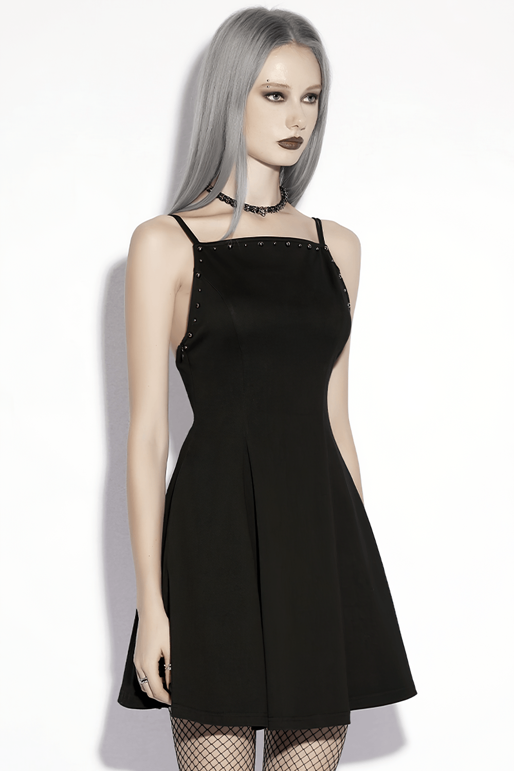 Alt Tag: Stylish Black Gothic Studded Strappy A-Line Mini Dress on model, square neck slip mini with metal studs and fishnet tights