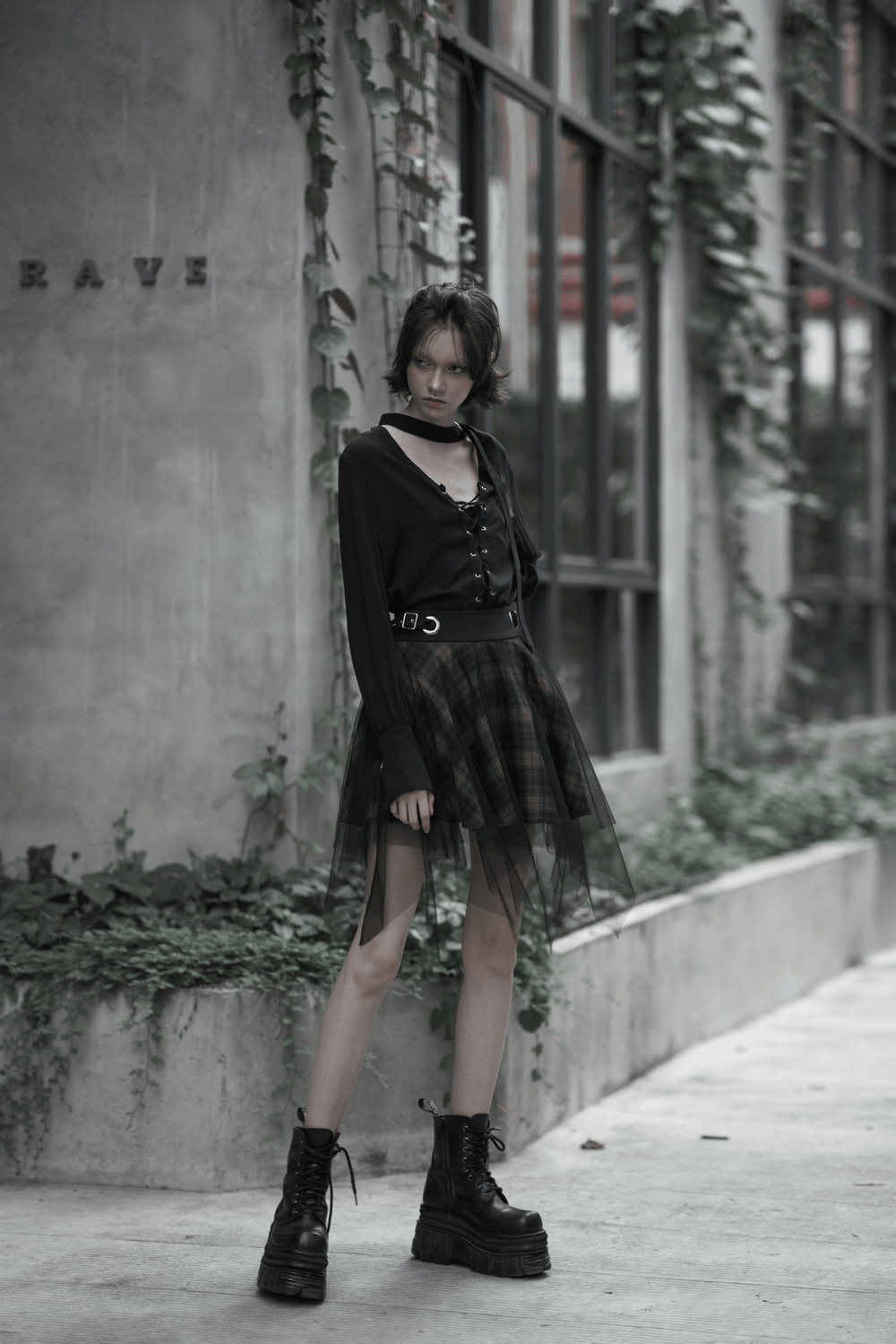 Edgy model in dark punk grunge plaid asymmetric mesh skirt and chunky boots, showcasing rebellious fashion style.