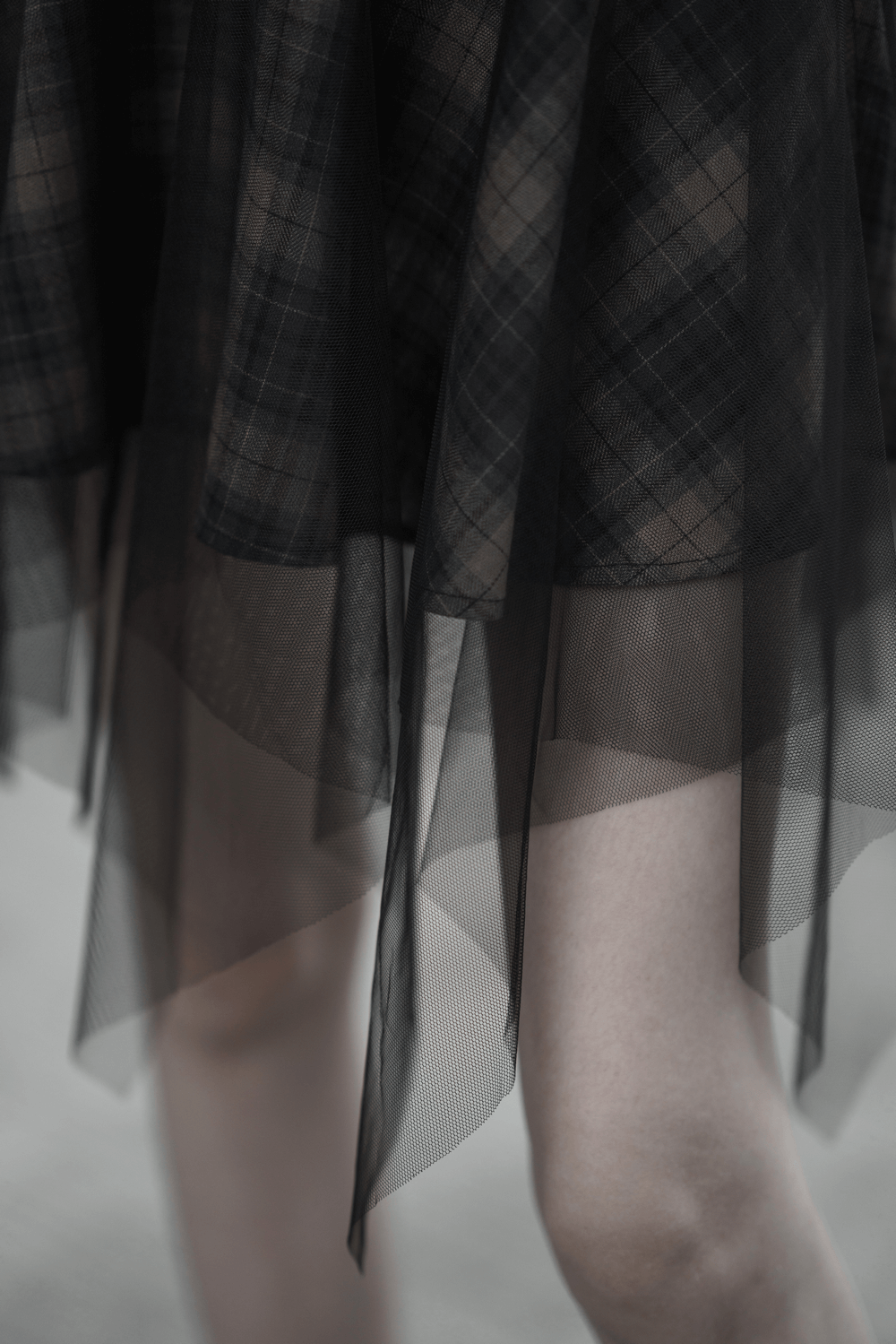 Stylish dark punk plaid mesh skirt with asymmetric hem, layering black netting and plaid patterns.