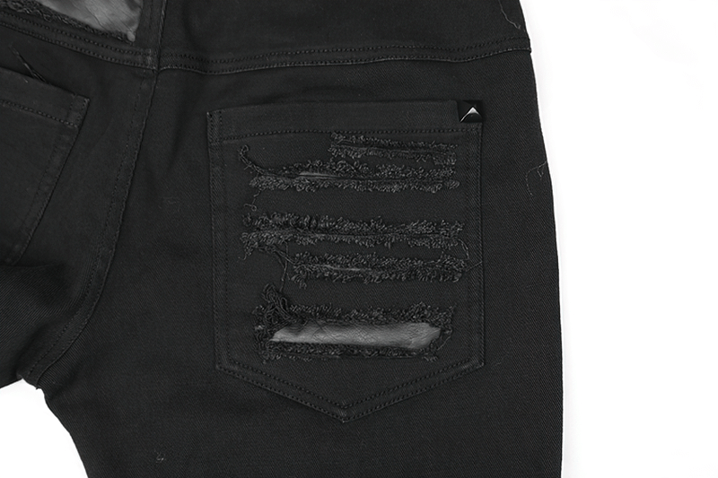 Close-up of stylish distressed black denim trousers with ripped patches and metallic stud detail.