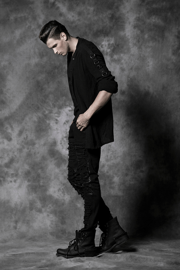 Stylish model in distressed knee-patch punk trousers and boots against a dramatic gray backdrop.