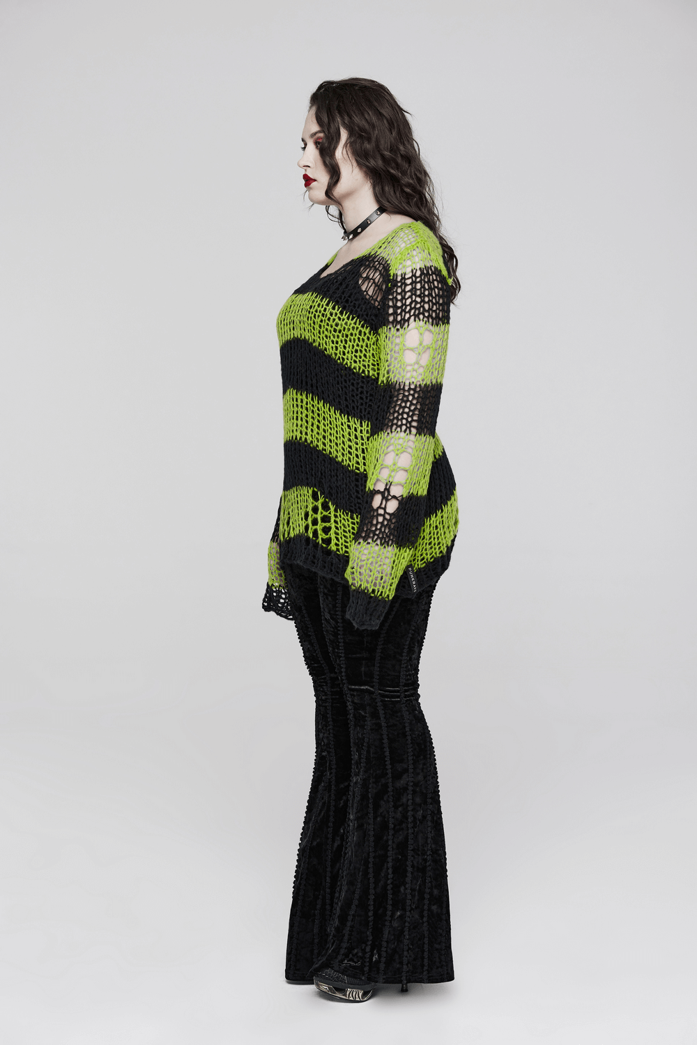 Side view of a stylish distressed striped mohair pullover sweater in black and neon green, paired with flared black pants.