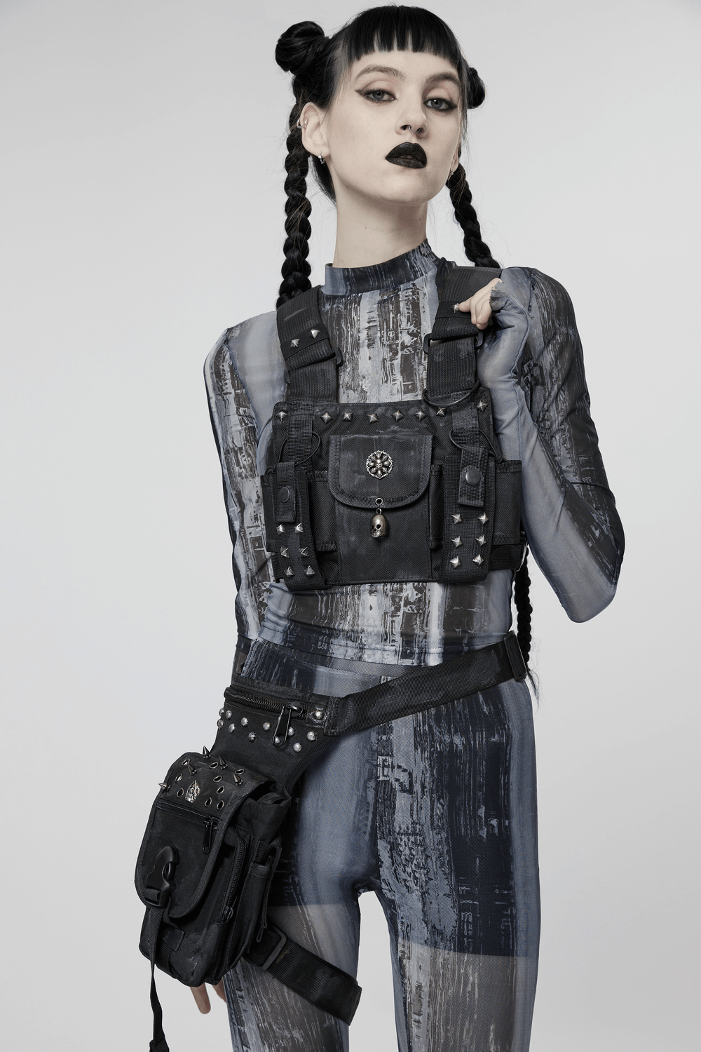 Stylish punk female model wearing a black skull studded strap bag and harness against a minimalistic background.