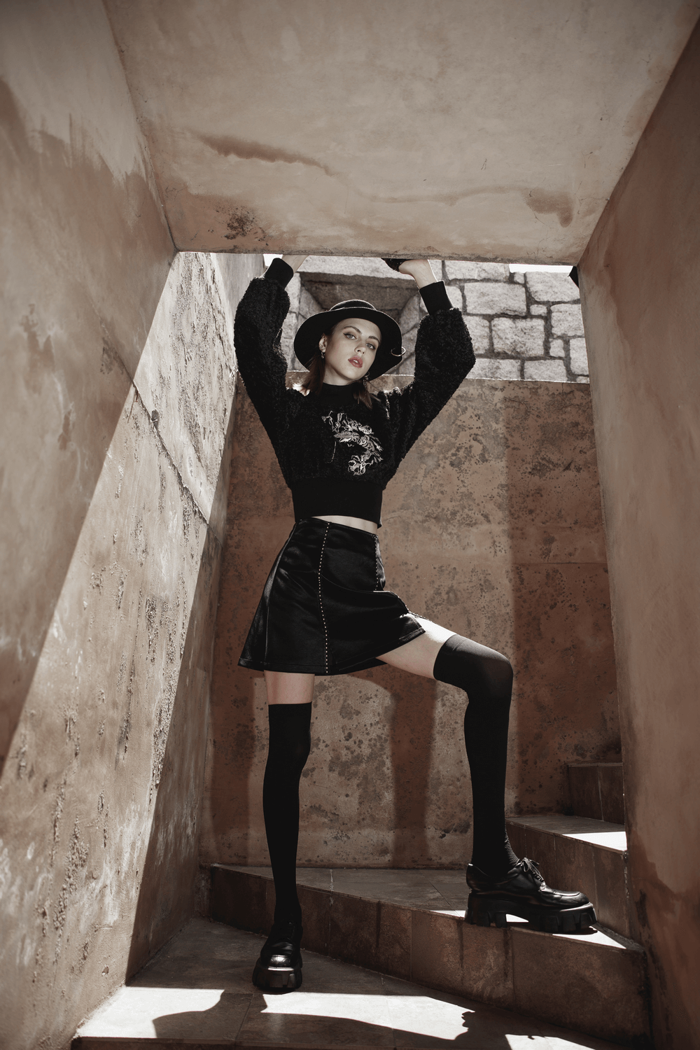 Stylish gothic mini skirt paired with a black sweater and hat, showcasing edgy fashion in a dramatic staircase setting.