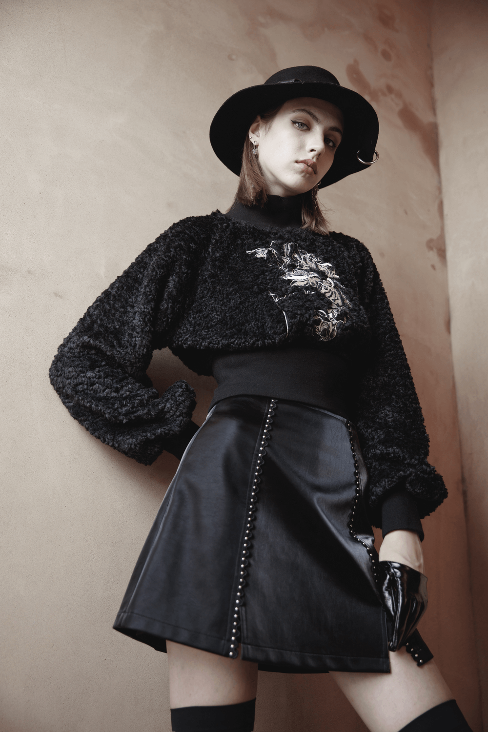 Stylish gothic mini skirt with lacing and rivet details, paired with a cozy black sweater and hat, exuding punk rave vibes.