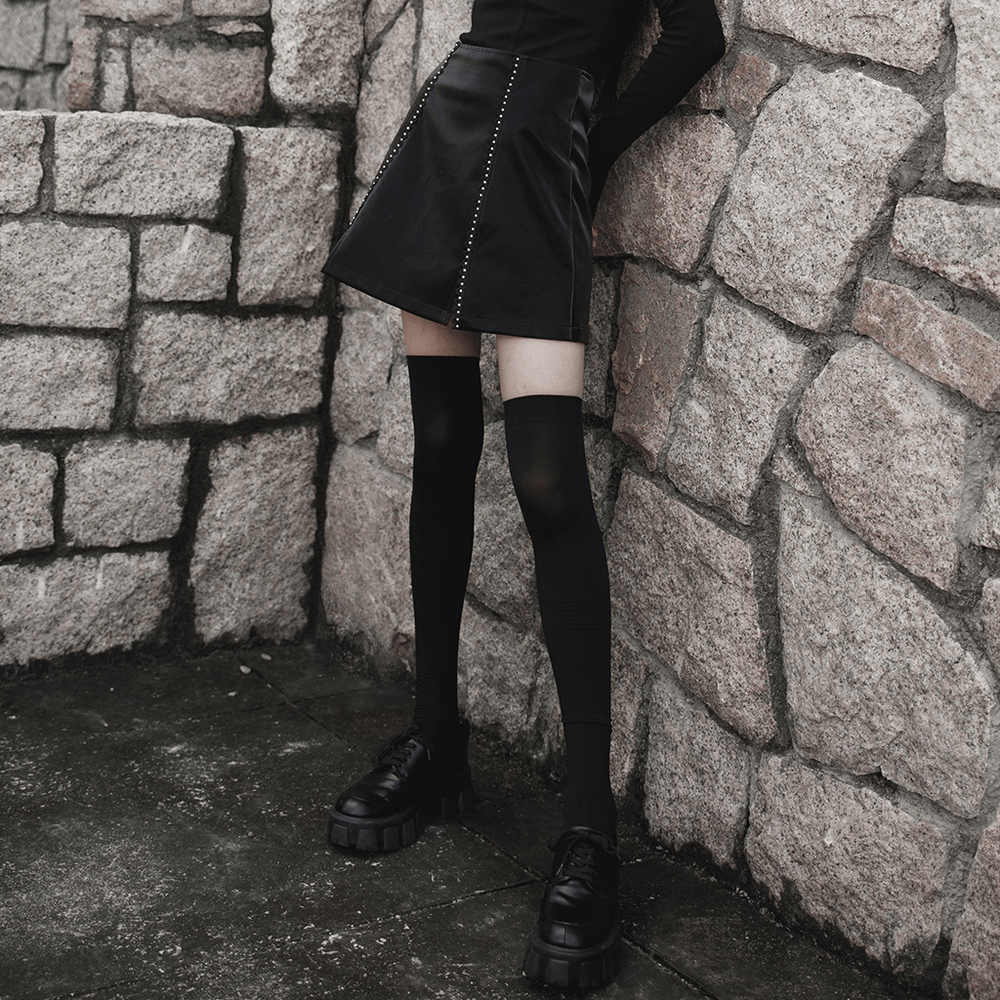 Gothic mini skirt with rivet details, paired with thigh-high socks and chunky shoes against stone wall backdrop.