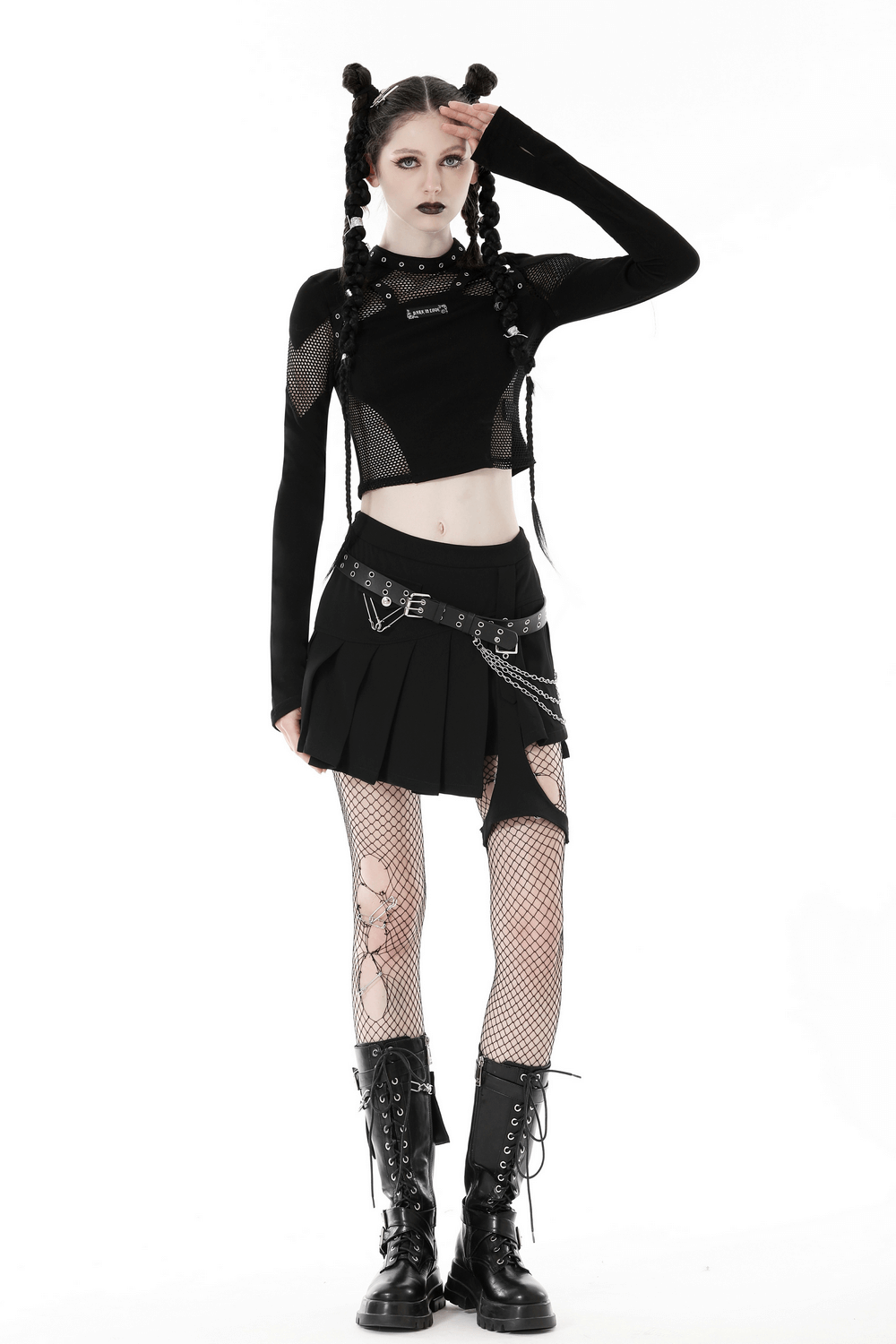 Edgy gothic woman in black mesh crop top and pleated skirt, showcasing rockstar style with fishnet tights and combat boots.