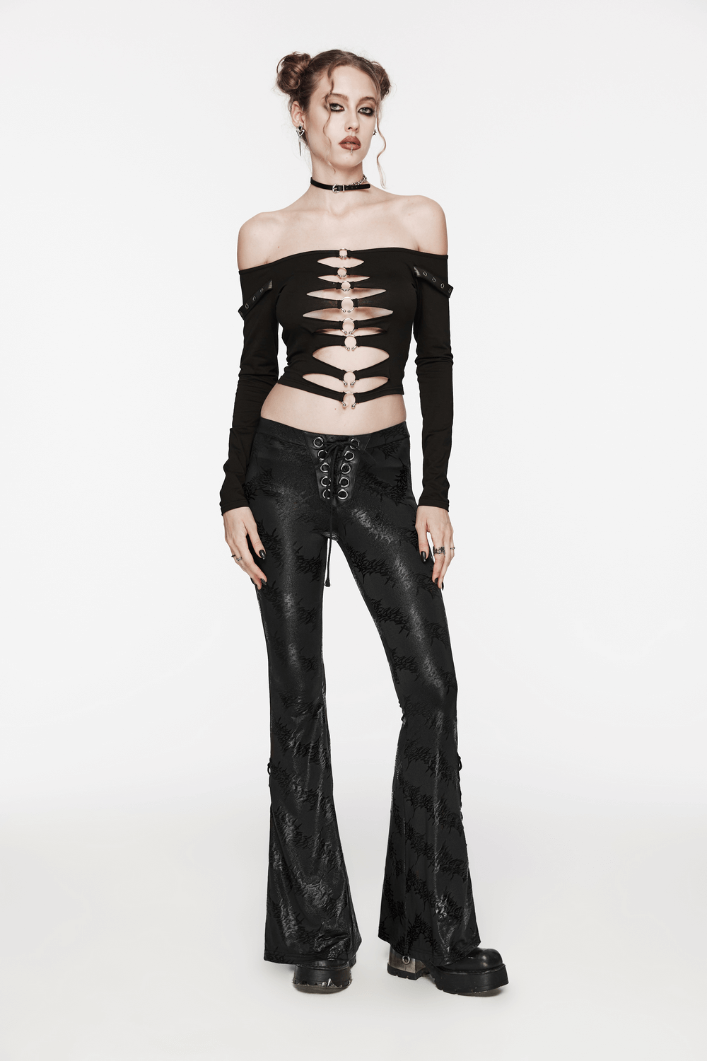 Chic woman in off-shoulder black top and stylish lace-up flared pants showcasing a punk-inspired look.