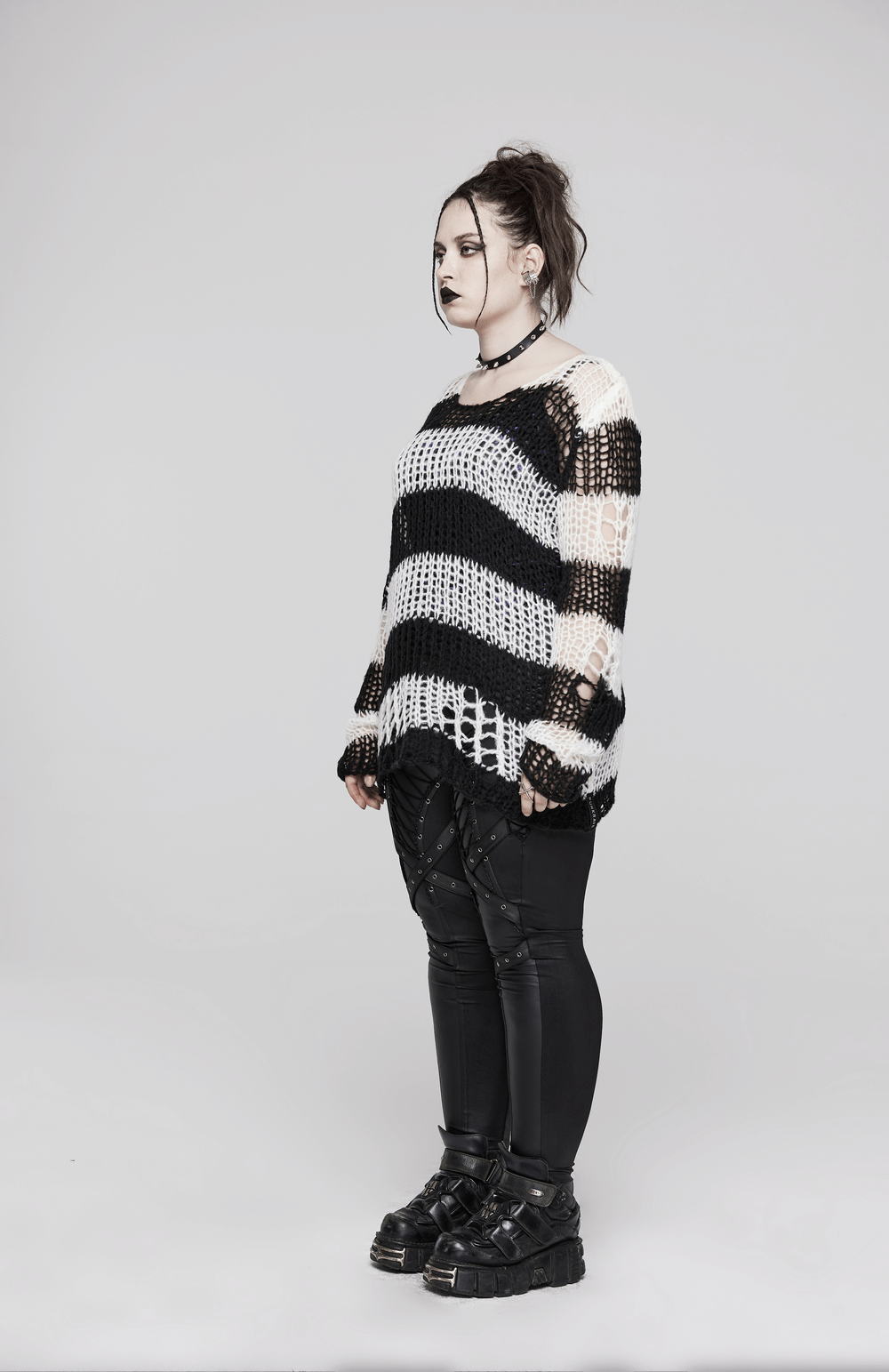 Fashion model wearing a stylish mohair striped pullover with irregular holes, paired with edgy black pants and chunky boots.