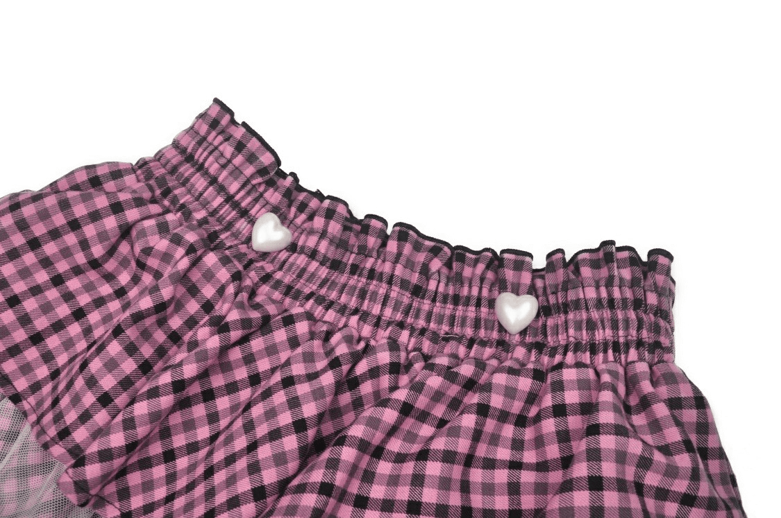 Close-up of stylish pink checkered skirt waistband with heart-shaped buttons and ruffles, perfect for a trendy look.