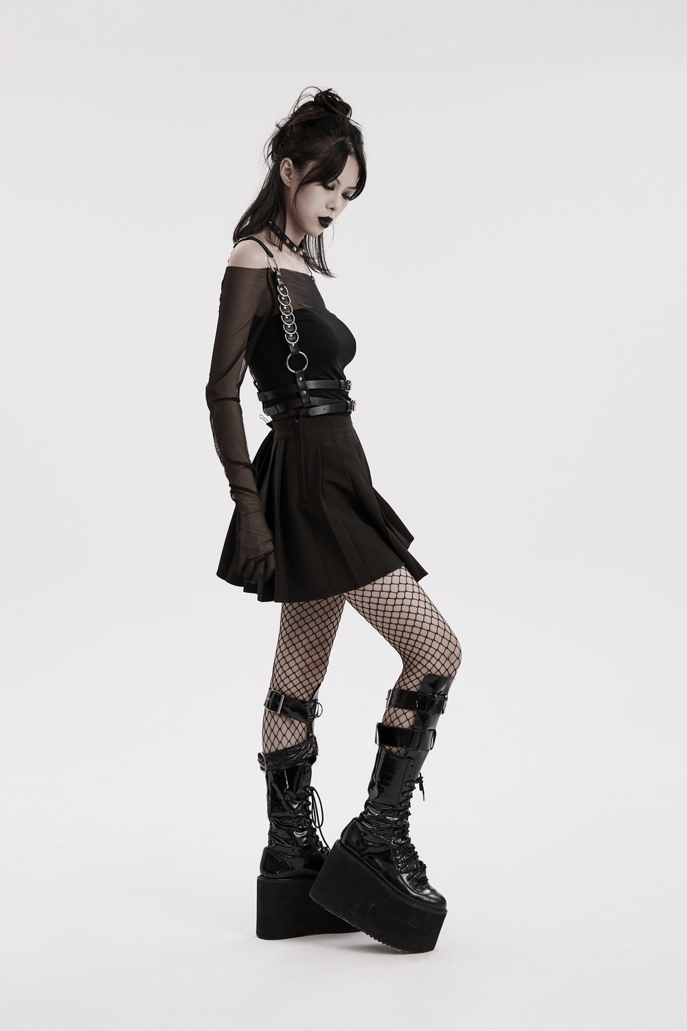 Woman in a black skirt and platform boots wearing an edgy punk harness with metal rings and adjustable straps, showcasing a bold style.