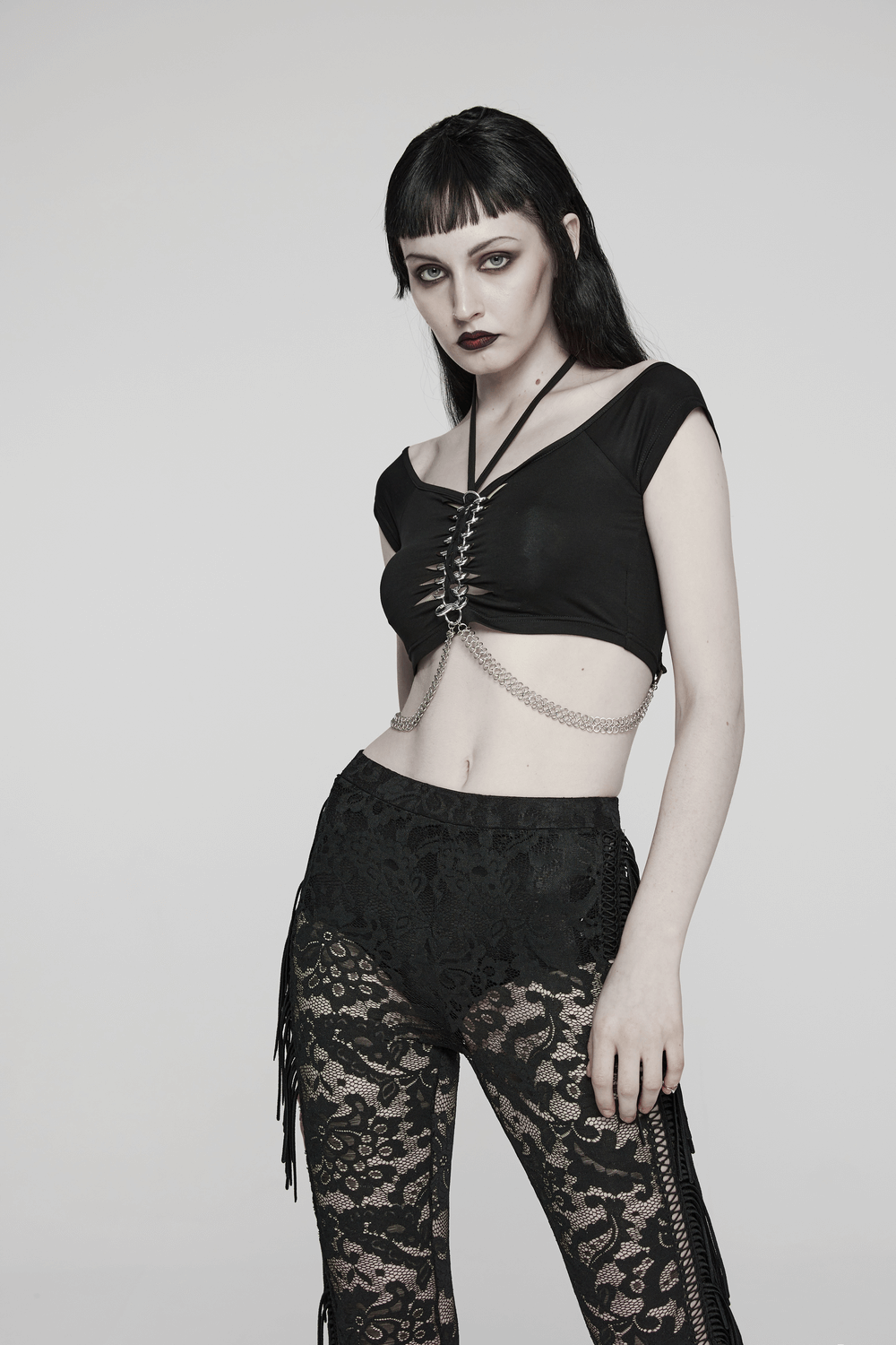 Edgy black halter neck crop top with chain detail, paired with lace pants for a punk-rock look.