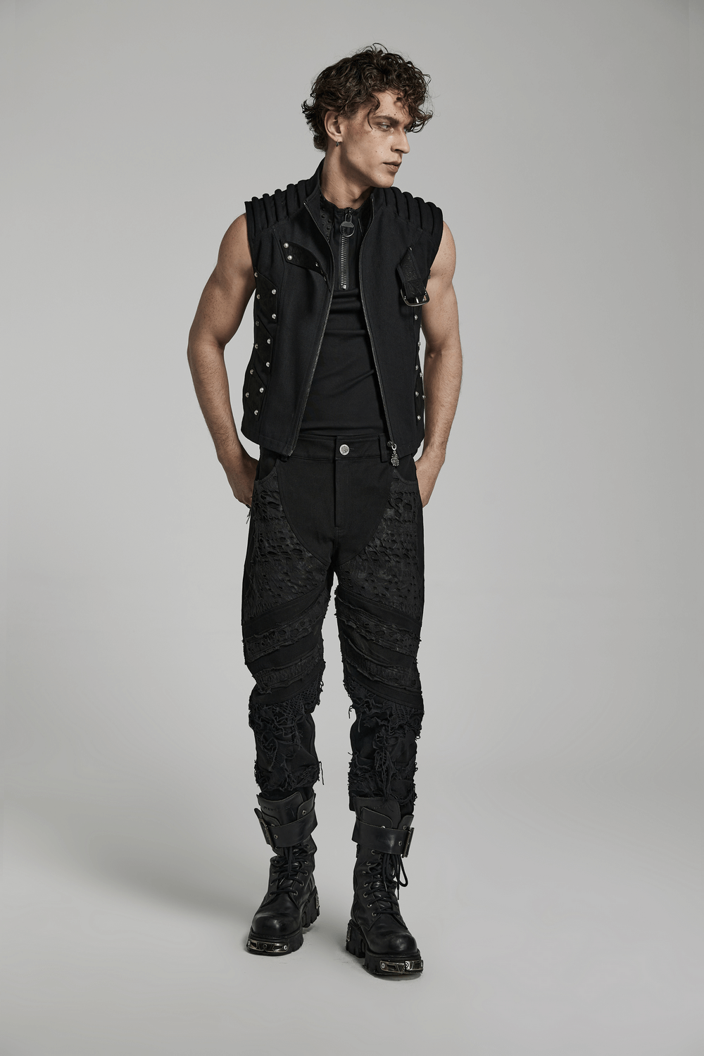 Stylish man in gothic ripped pants and fitted vest, showcasing edgy streetwear fashion in black.