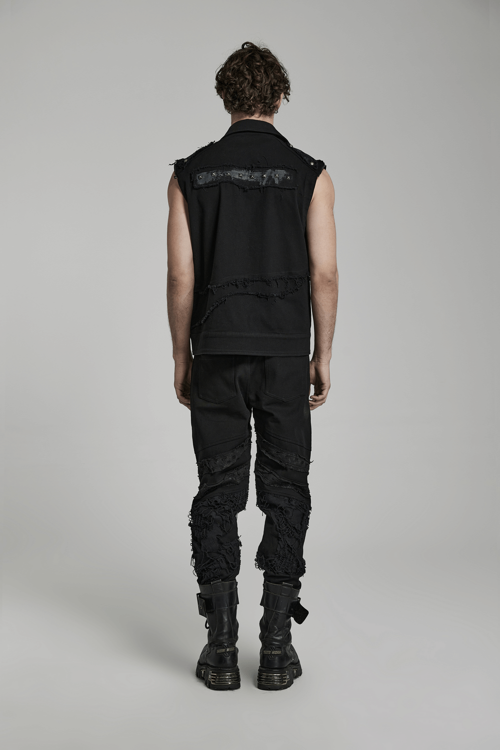 Rear view of a man in stylish ripped black gothic trousers and sleeveless vest, showcasing edgy streetwear fashion.