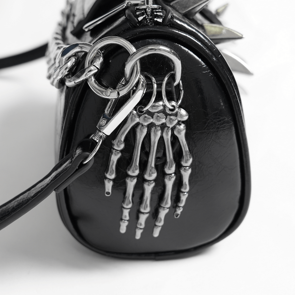 Close-up of stylish black shoulder bag featuring bold silver skeleton hand charm and sleek design.