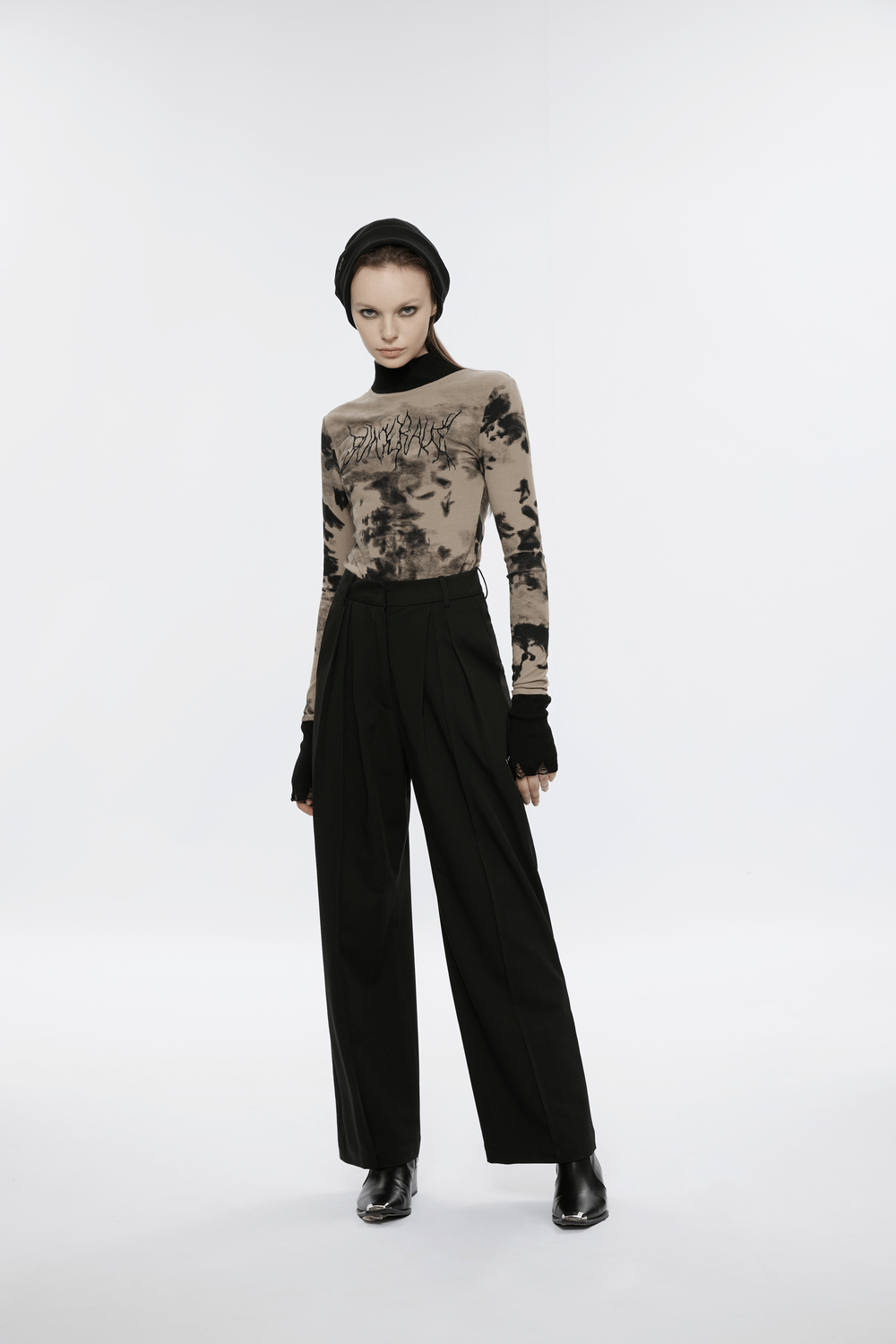 Model wearing a stylish tie dye turtleneck top with ripped cuffs, paired with black high-waisted trousers.