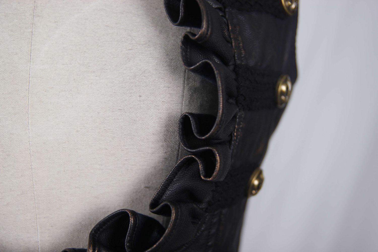 Close-up of the frilly edge and gold buttons on a stylish women's steampunk PU leather waistcoat.
