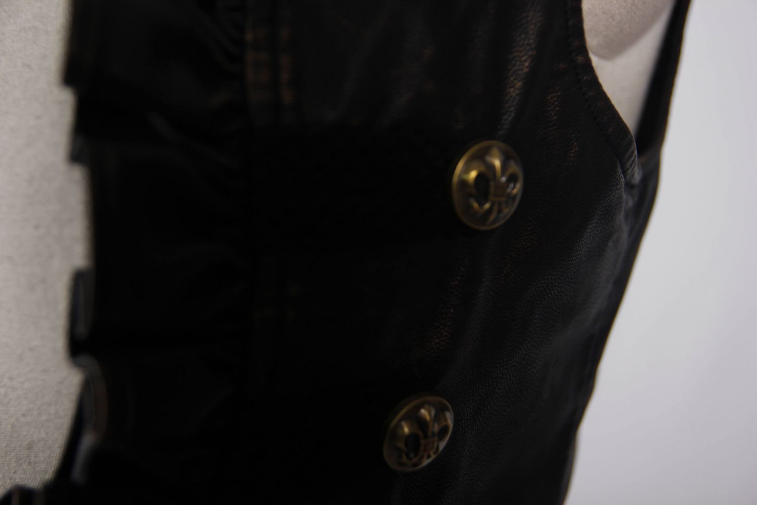 Close-up of stylish women's black PU leather steampunk waistcoat with gold buttons and frills.