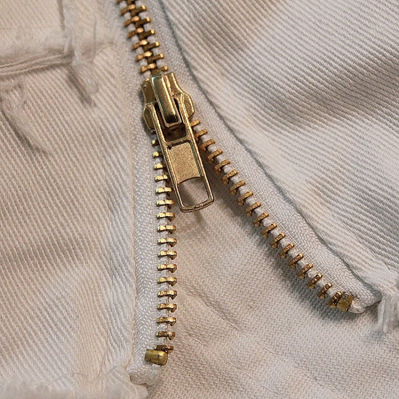 Close-up of a stylish gold zipper on white denim shorts, showcasing quality craftsmanship and trendy design.
