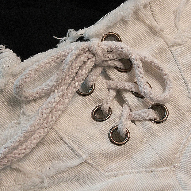 Close-up of white denim short shorts with stylish lacing and metal eyelets, showcasing grunge fashion details.