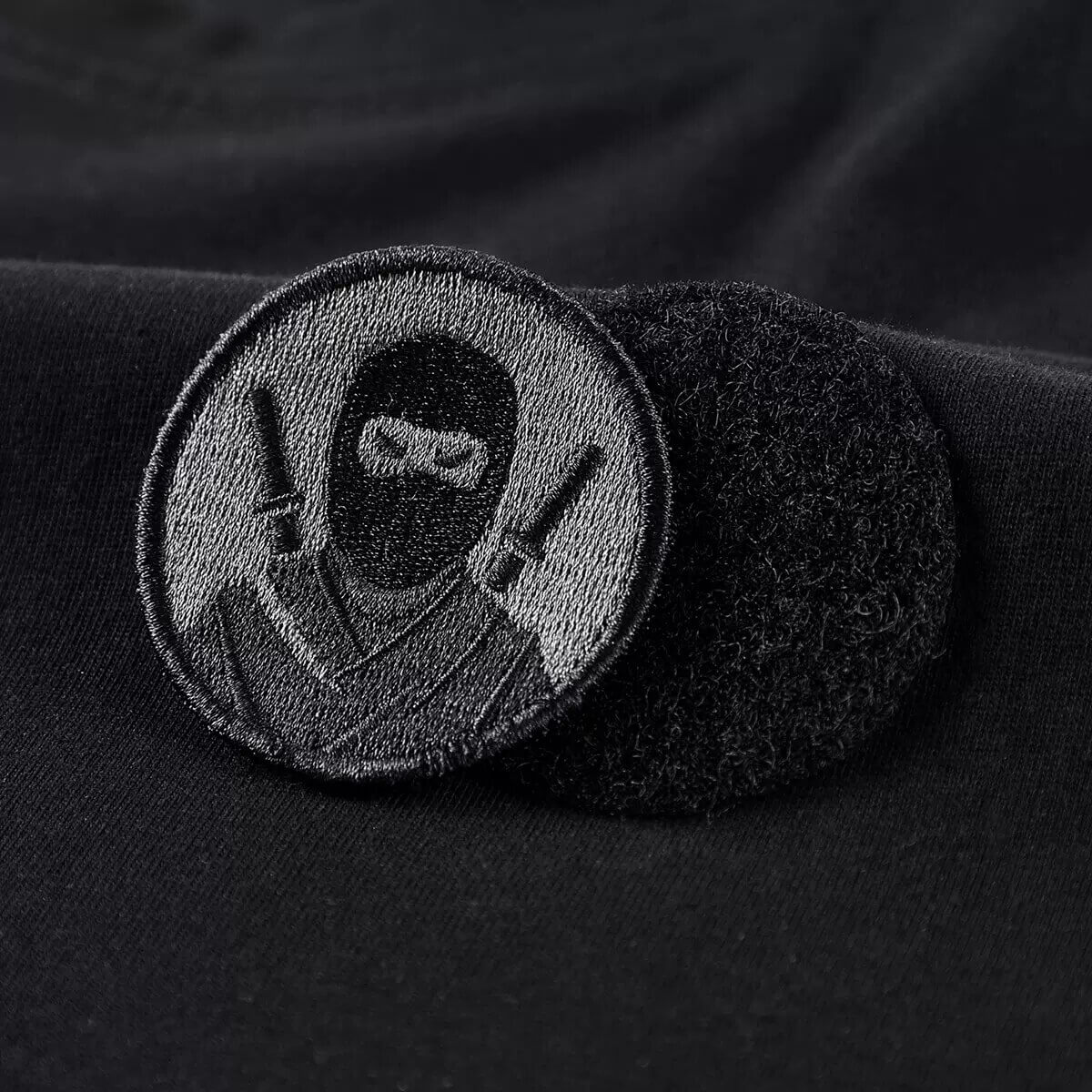 Black ninja patch with swords on a fabric background, perfect for tactical style clothing.