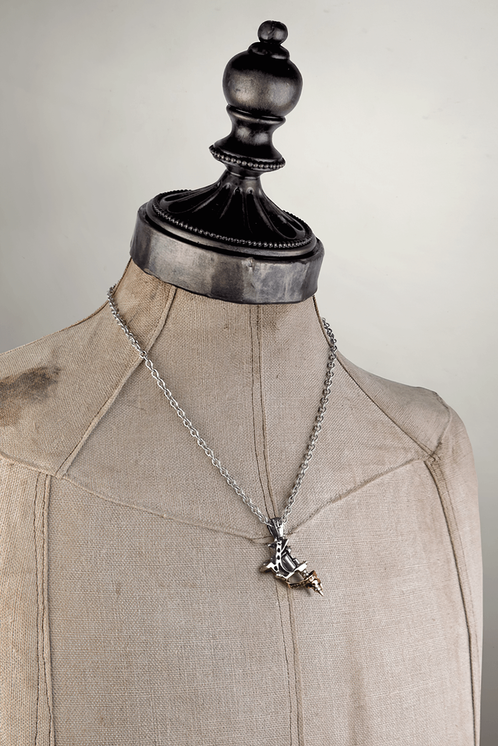 Stylish antique silver tattoo gun pendant necklace displayed on a vintage mannequin, featuring detailed engraving and a copper scroll.