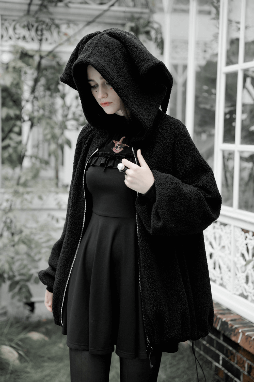 Trendy black hooded jacket with playful clown hat design, cozy teddy fleece for fall, styled with black dress.
