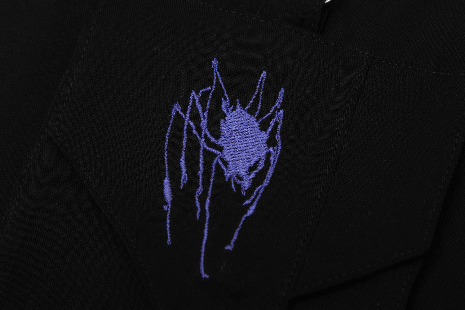 Close-up of purple spider embroidery on black fabric, showcasing edgy gothic style.