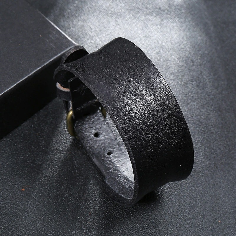 Unisex wide black leather bracelet on a textured surface, showcasing stylish punk fashion and genuine leather craftsmanship.