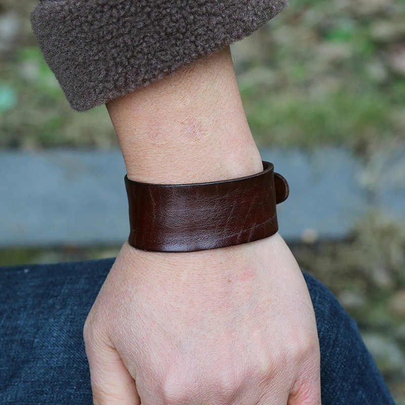 Close-up of a person's wrist wearing a unisex wide brown leather bracelet, showcasing punk style fashion.