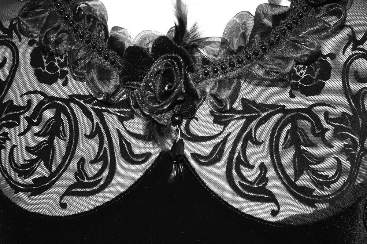 Close-up of intricate filigree patterns on a velvet black dress, featuring a floral design and elegant ruffles.