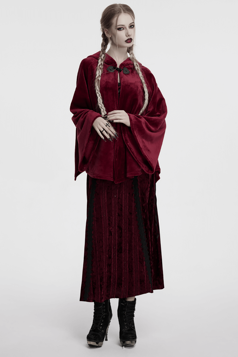 Stylish model in a dark red velvet hooded cape with flowing sleeves and matching skirt, showcasing a mystical fashion look.