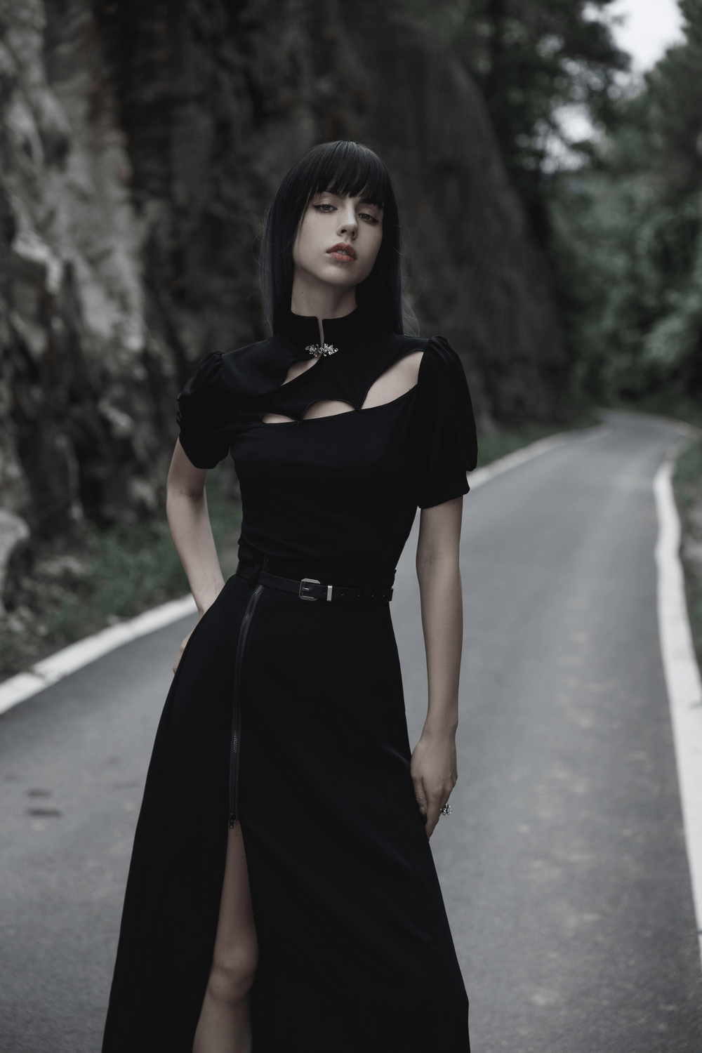Stylish woman in black A-line midi skirt with zipper detail, standing confidently on a scenic road.