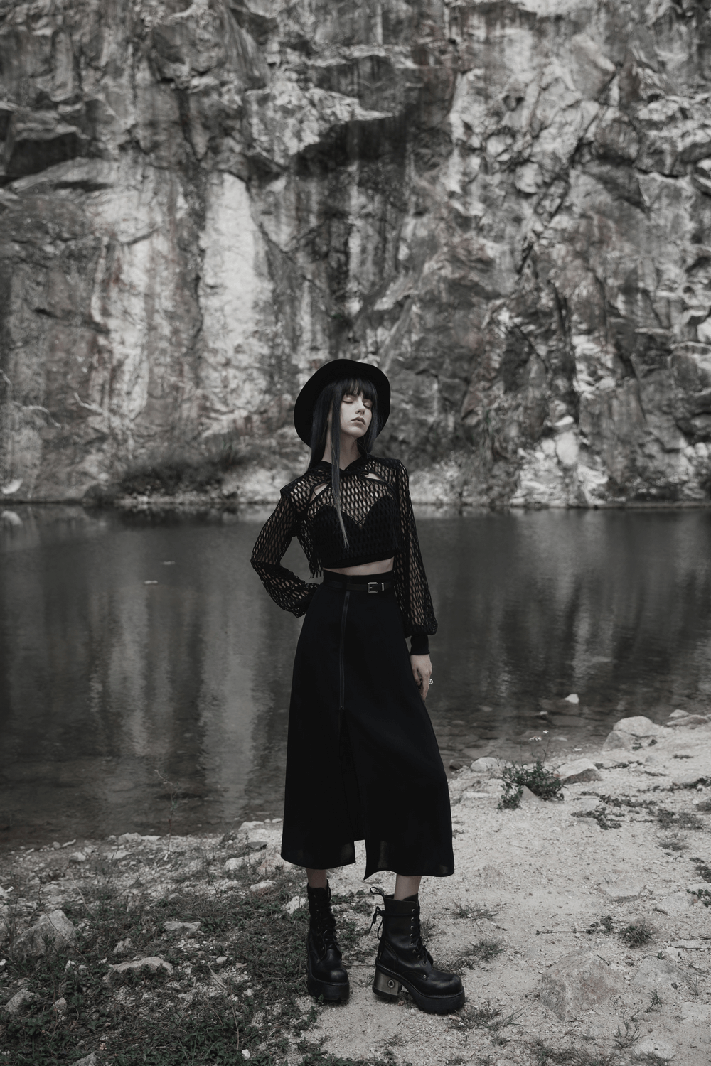 Stylish model in black A-line midi skirt with side zipper, standing by a serene water body, showcasing modern elegance.