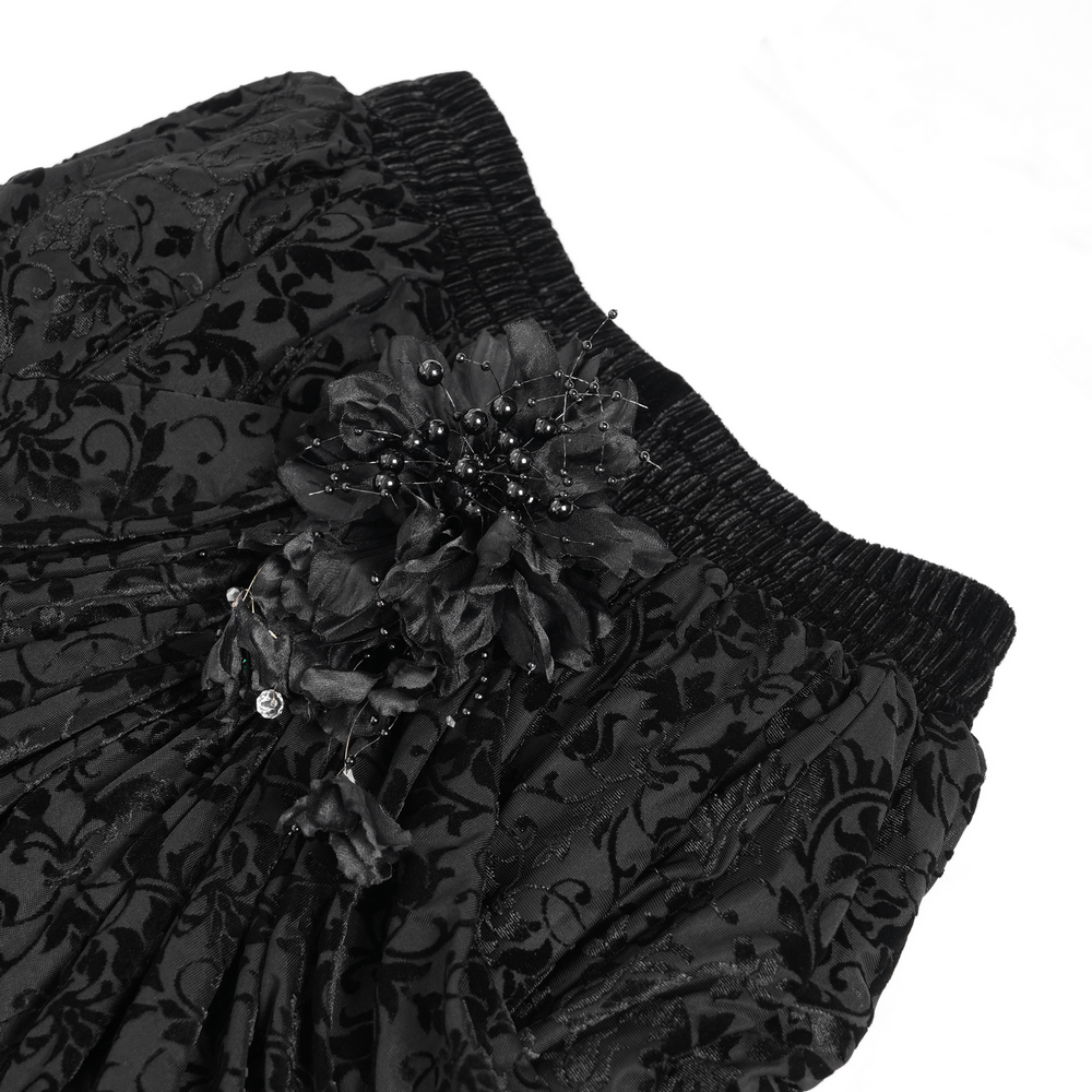Close-up of a black gothic skirt showcasing floral appliqués and pleated velvet fabric.