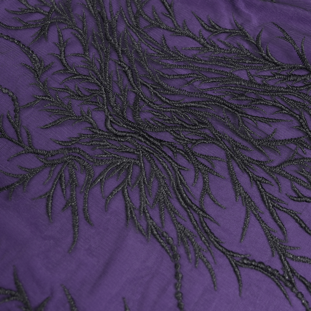 Close-up of black embroidered floral design on deep purple fabric, showcasing gothic elegance.
