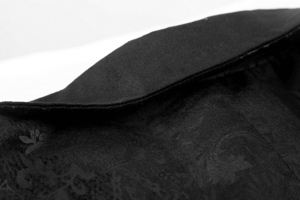 Close-up of luxurious black fabric featuring intricate dark prints and velvet trim of a Victorian gothic waistcoat.