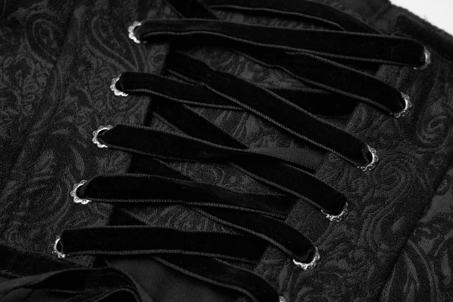 Close-up of black brocade corset showing intricate ornamental eyelet lacing details and elegant fabric texture.