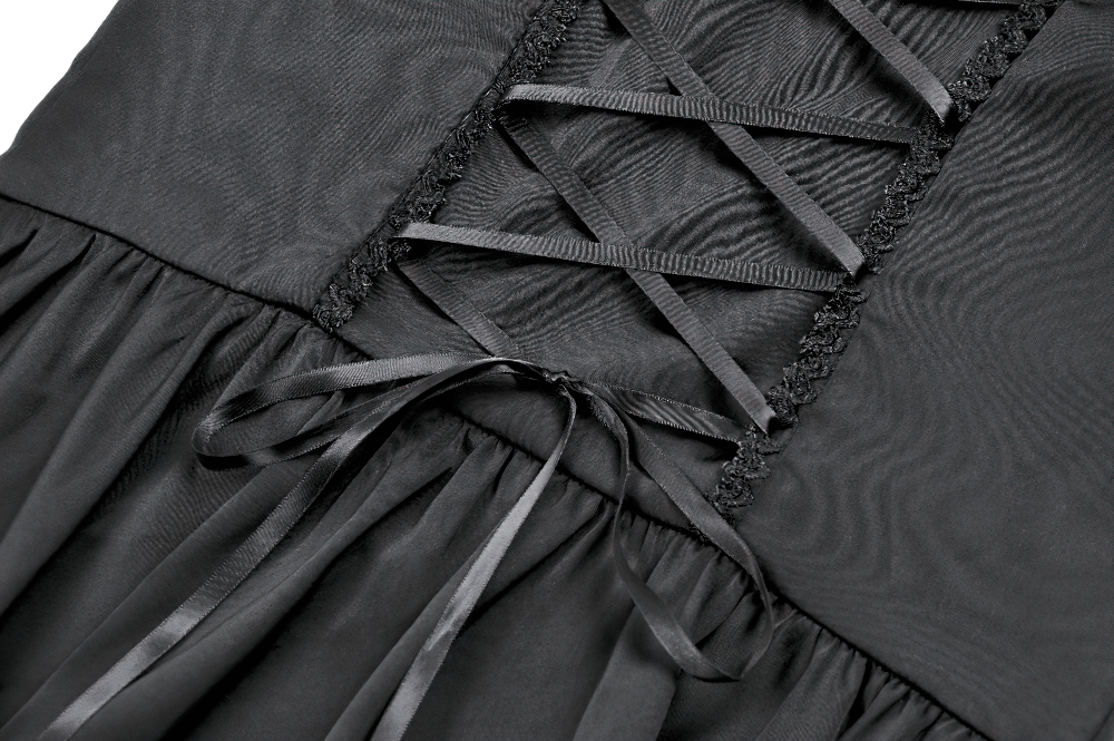 Close-up of the lace-up detail and ruffled hem of a Victorian-inspired black satin dress.