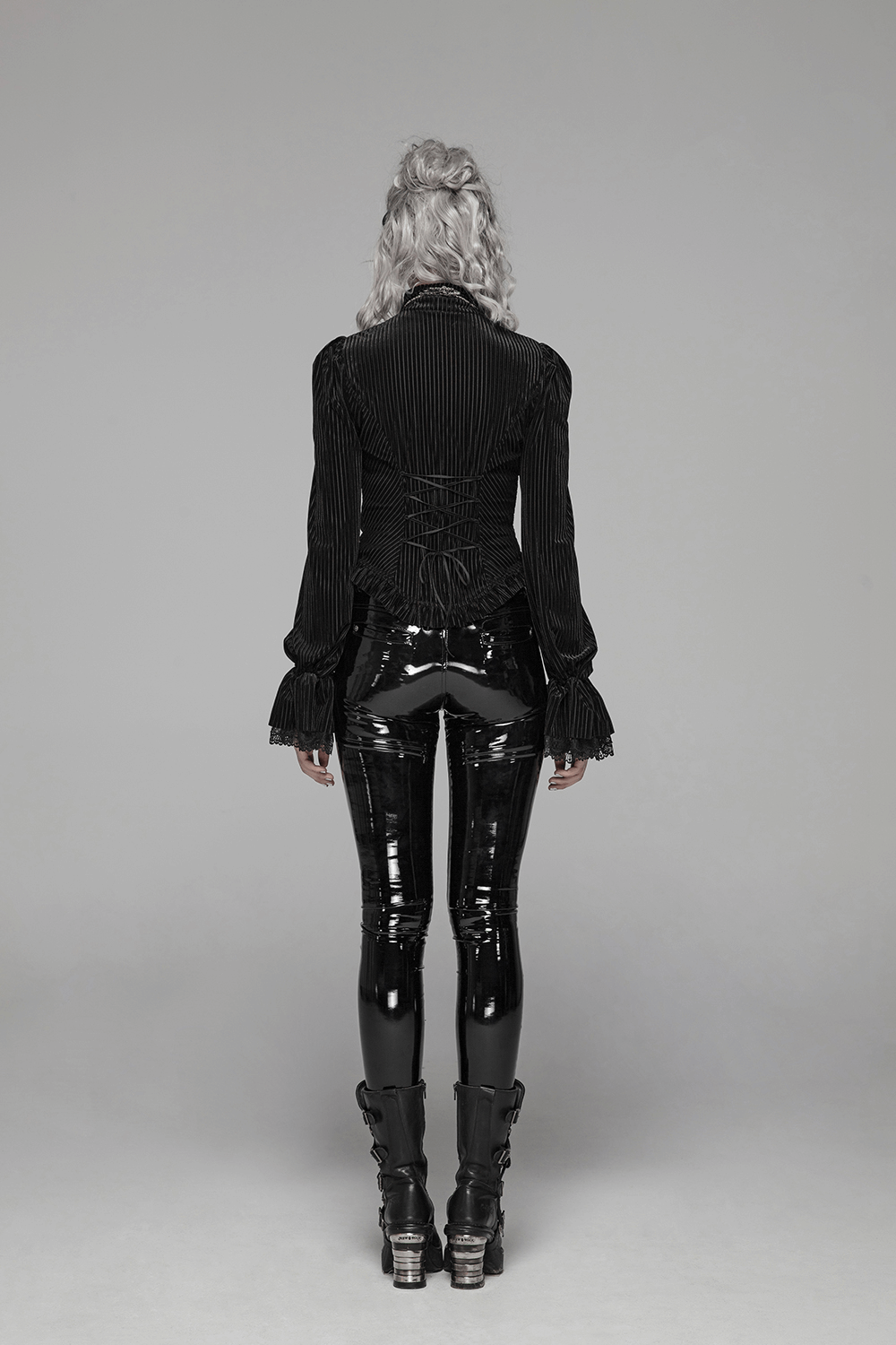 Back view of a lady wearing a Victorian-inspired black velvet corset blouse with glossy pants.