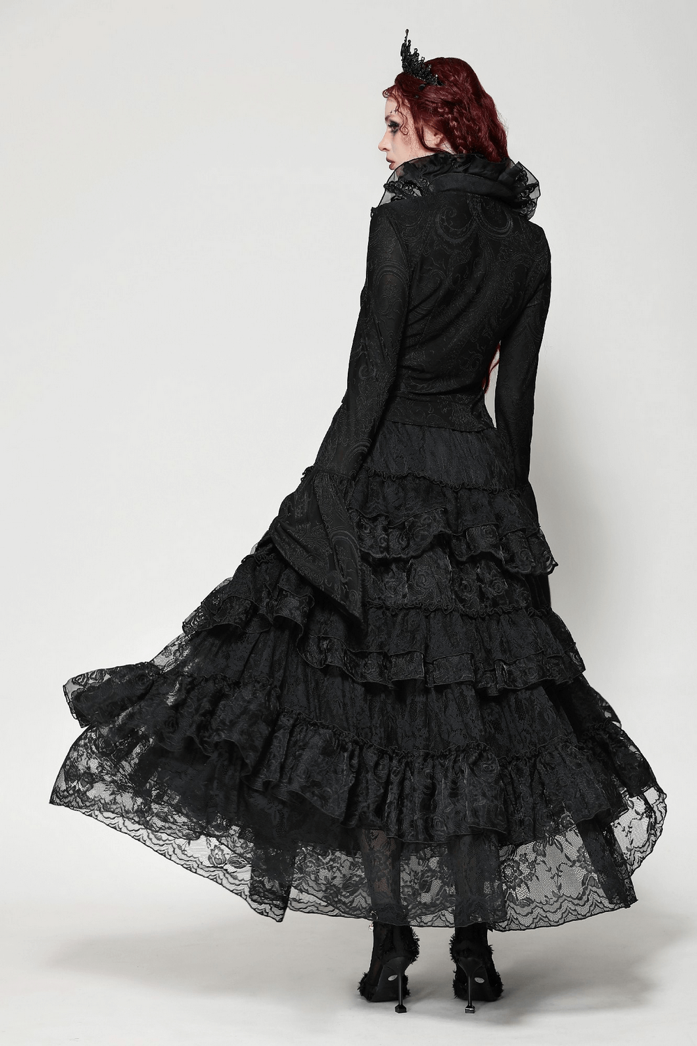 Elegant gothic model in a black lace dress with ruffled layers and flared sleeves, showcasing a dramatic back view.