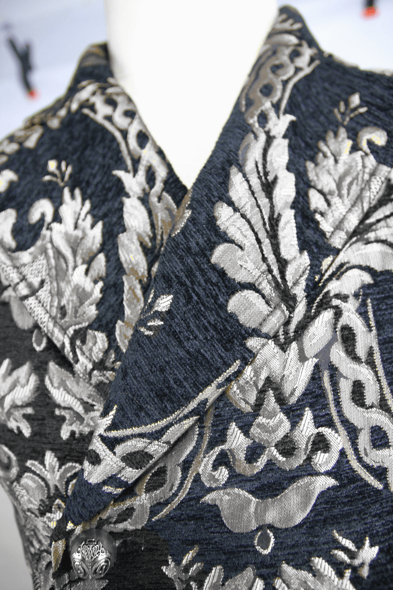 Close-up of a vintage black waistcoat with intricate silver filigree detailing for gothic male fashion.