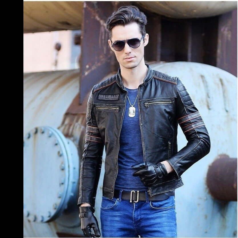 Stylish man in a black leather biker jacket with sunglasses, posing confidently against an industrial backdrop.