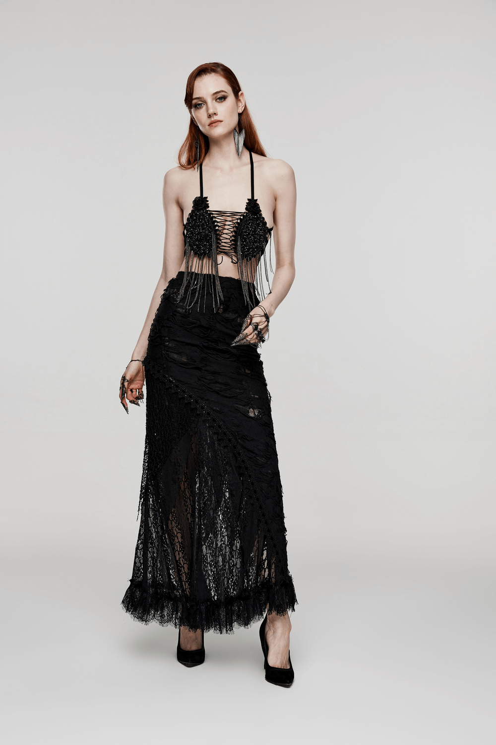 Model showcasing a dramatic black gothic outfit with intricate lace details and a striking tassel design.