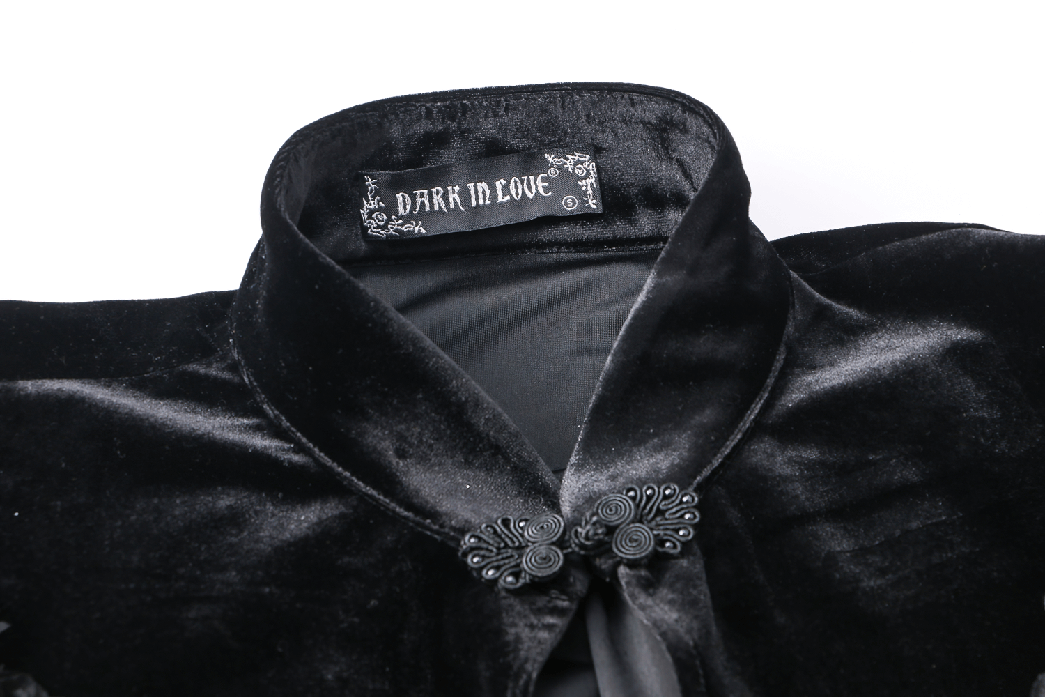 Close-up of a black velvet capelet collar with 'DARK IN LOVE' label and ornate fasteners.