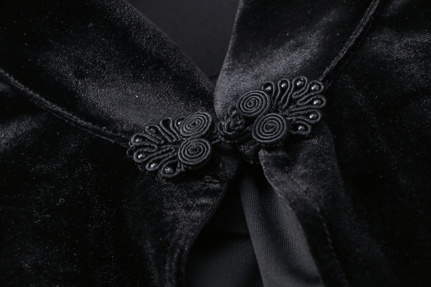 Close-up of intricate black velvet capelet fastening with elegant lace detail and ornate pearls.